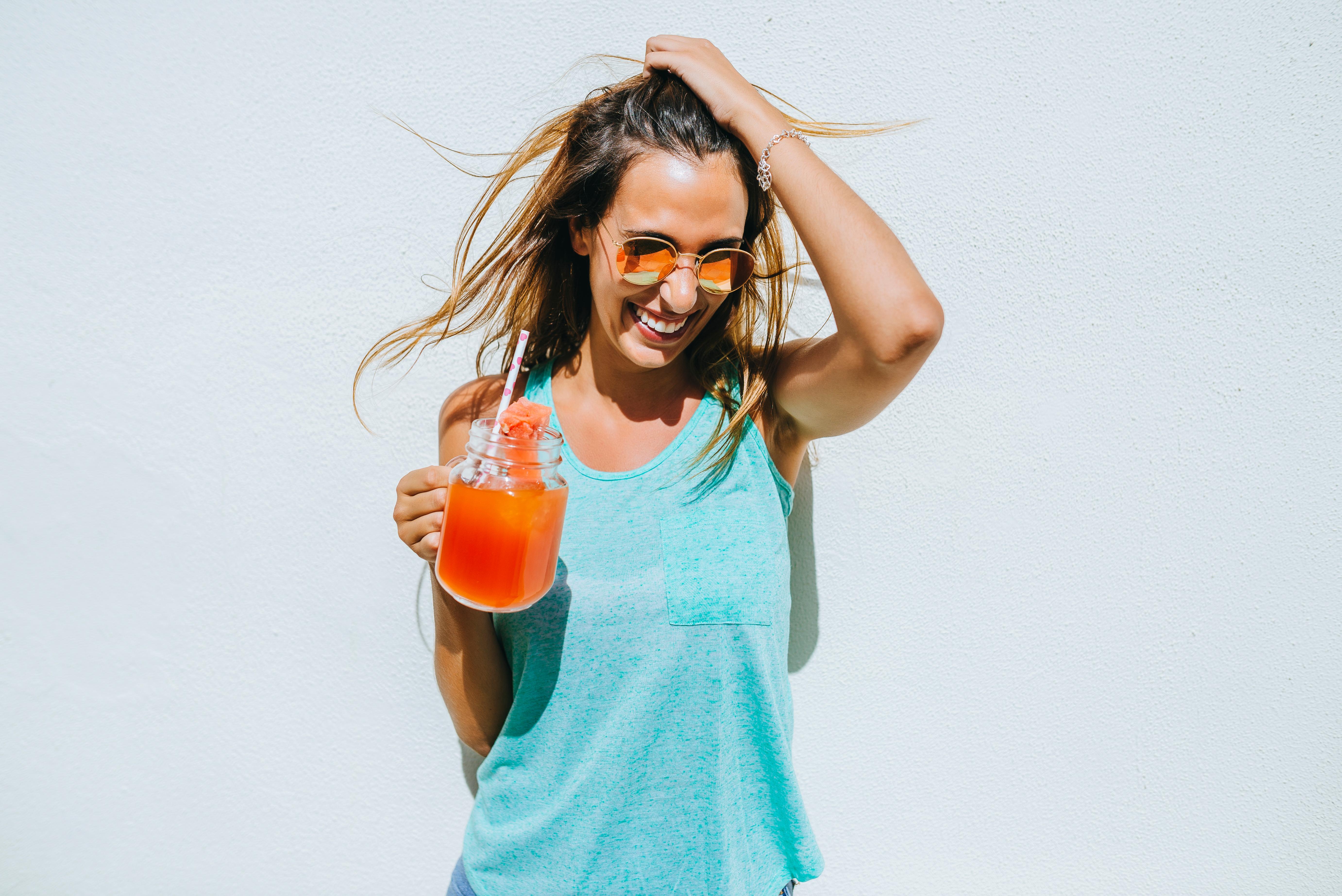 Happy young woman holding watermelon drink in front of white wall
