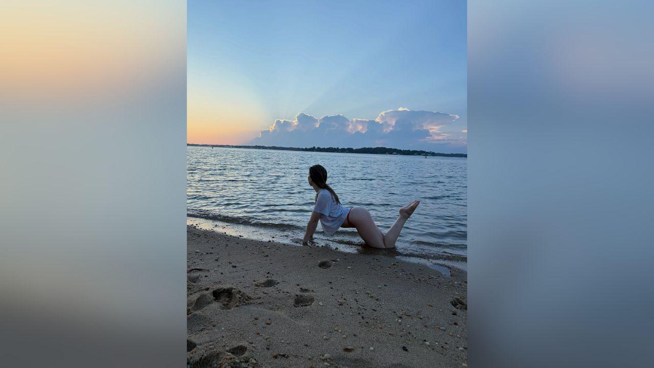 image of Gabby Windey posed in a white T-shirt and bikini bottoms while playing around near the shoreline.