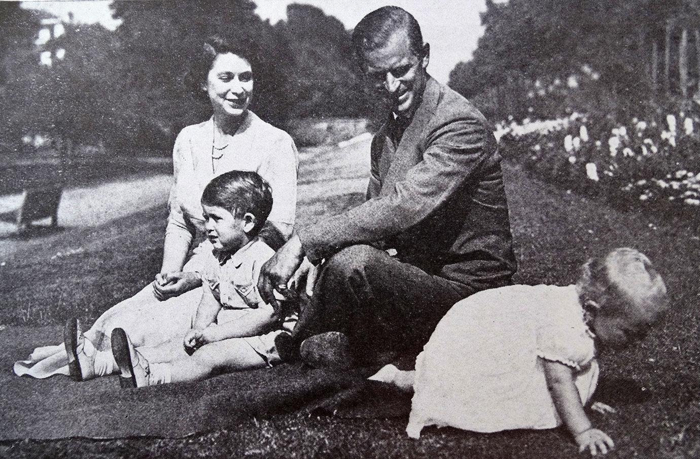 Princess Elizabeth and her husband pose with their children in the gardens of their home, Clarence House. Princess Anne, tired of photographers, crawls towards the flowers.