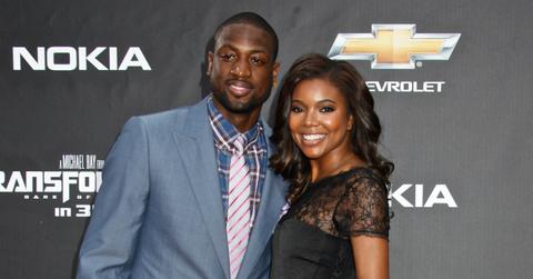 Dwayne Wade, in a blue jacket, white pants, and red shoes, poses with Gabrielle Union who wears a black dress and black wedges.