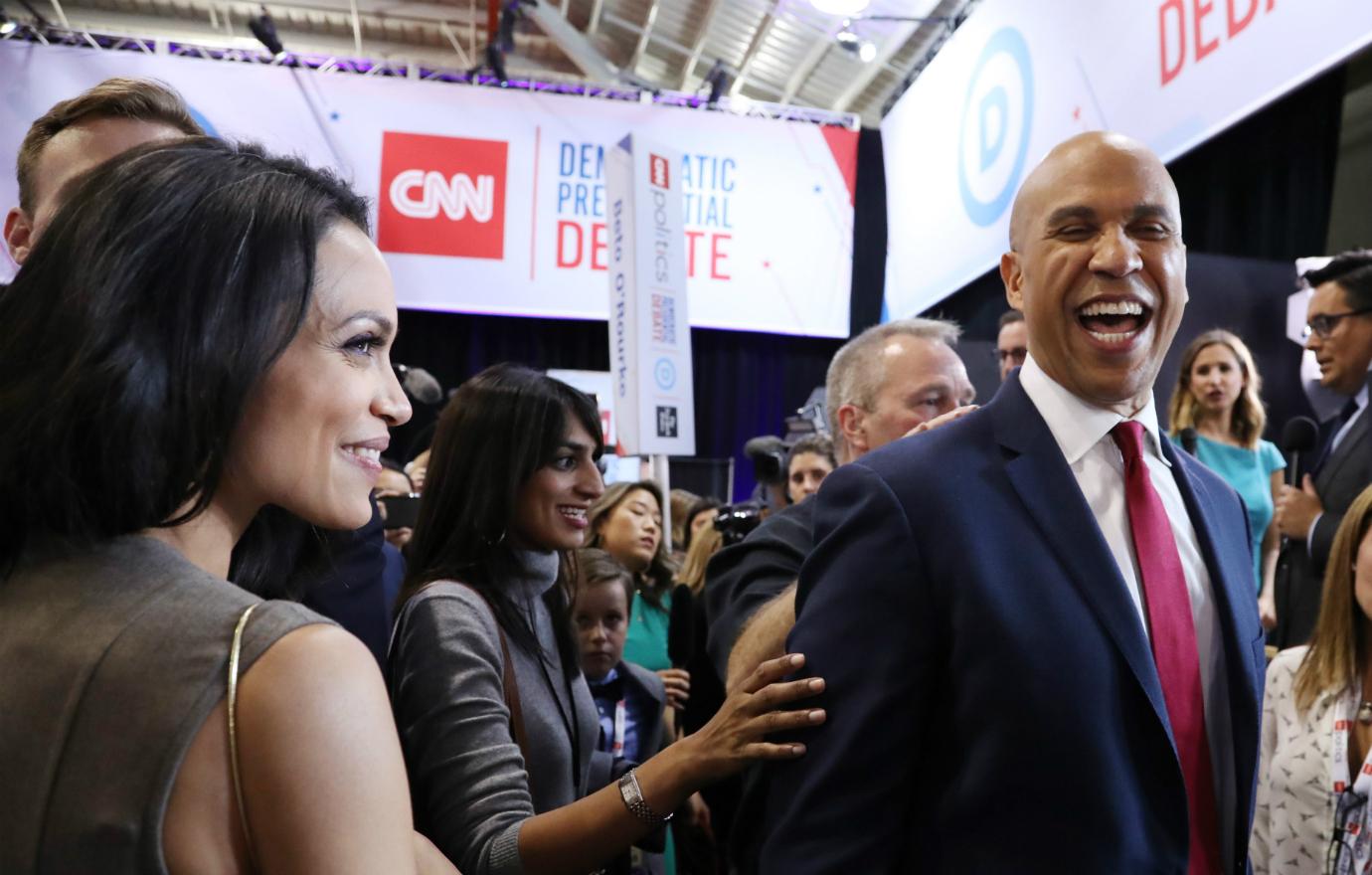 Cory Booker, in suit and red tie, laughs while a beaming Rosario Dawson, in a lime green dress, looks on.