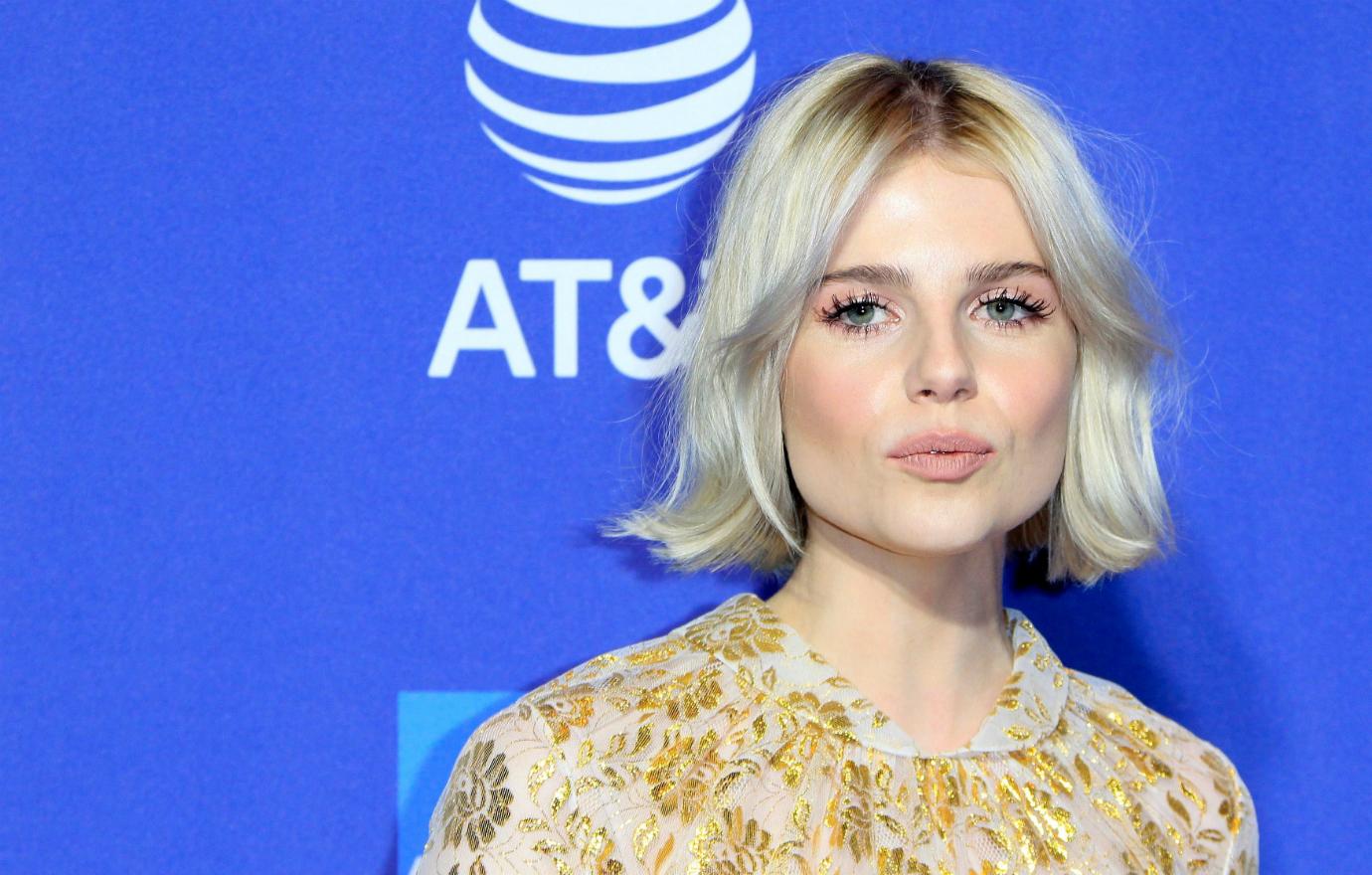 Lucy Boynton wears a patterened dress and stands on the red carpet.