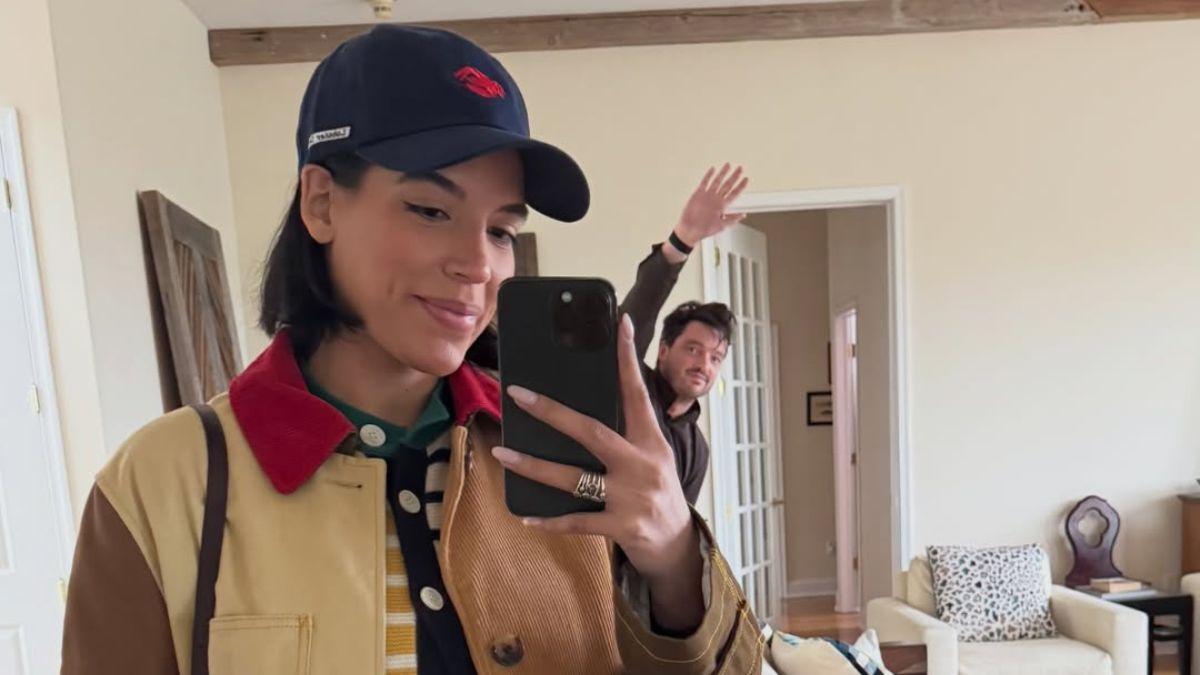 Image of Olivera as she snaps a mirror selfie while Heavey playfully waves in the background.
