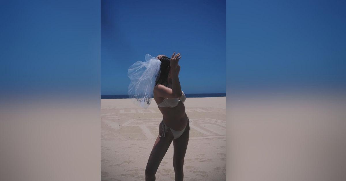 image of The singer stunned in a white bikini with a playful bridal veil on the beach.