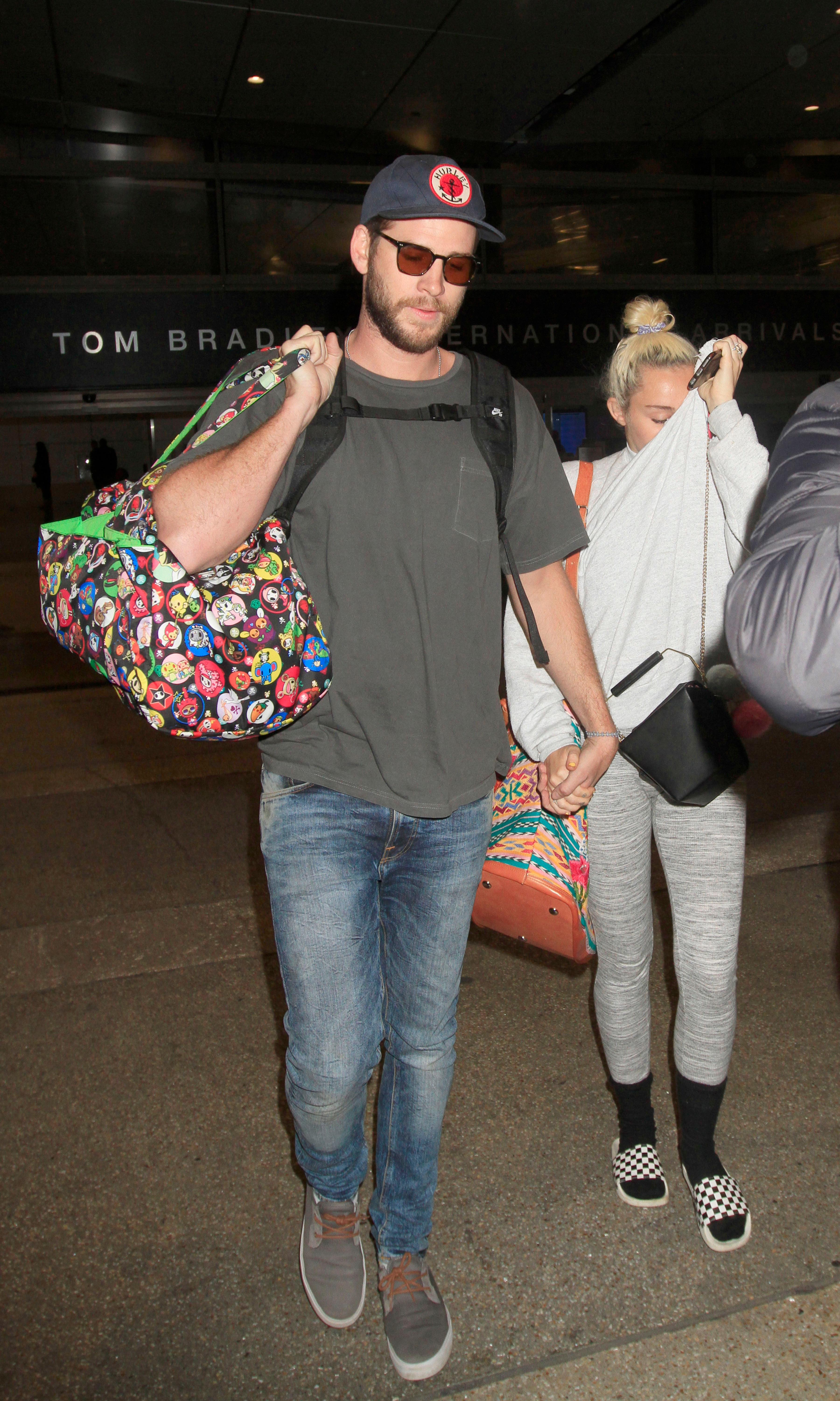 Miley Cyrus spotted with a ring on her left ring finger as she &amp; Liam Hemsworth are spotted holding hands arriving back in Los Angeles.