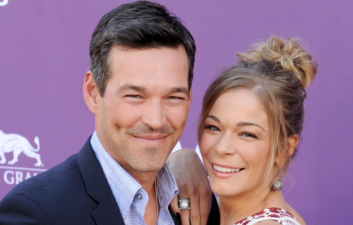 Eddie Cibrian wears a dark jacket and unbuttoned shirt with LeAnn Rimes, hair in an updo, wearing a white and red dress at the 2012 Academy of country Music Awards.