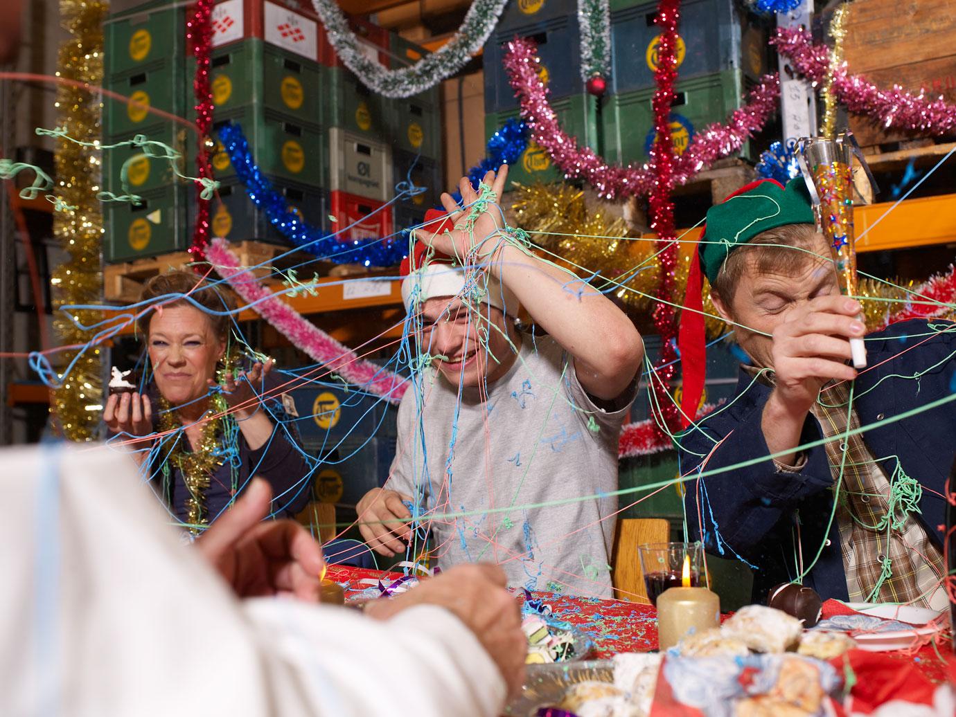 Three people covered in party streamers laughing at charismas table in warehouse