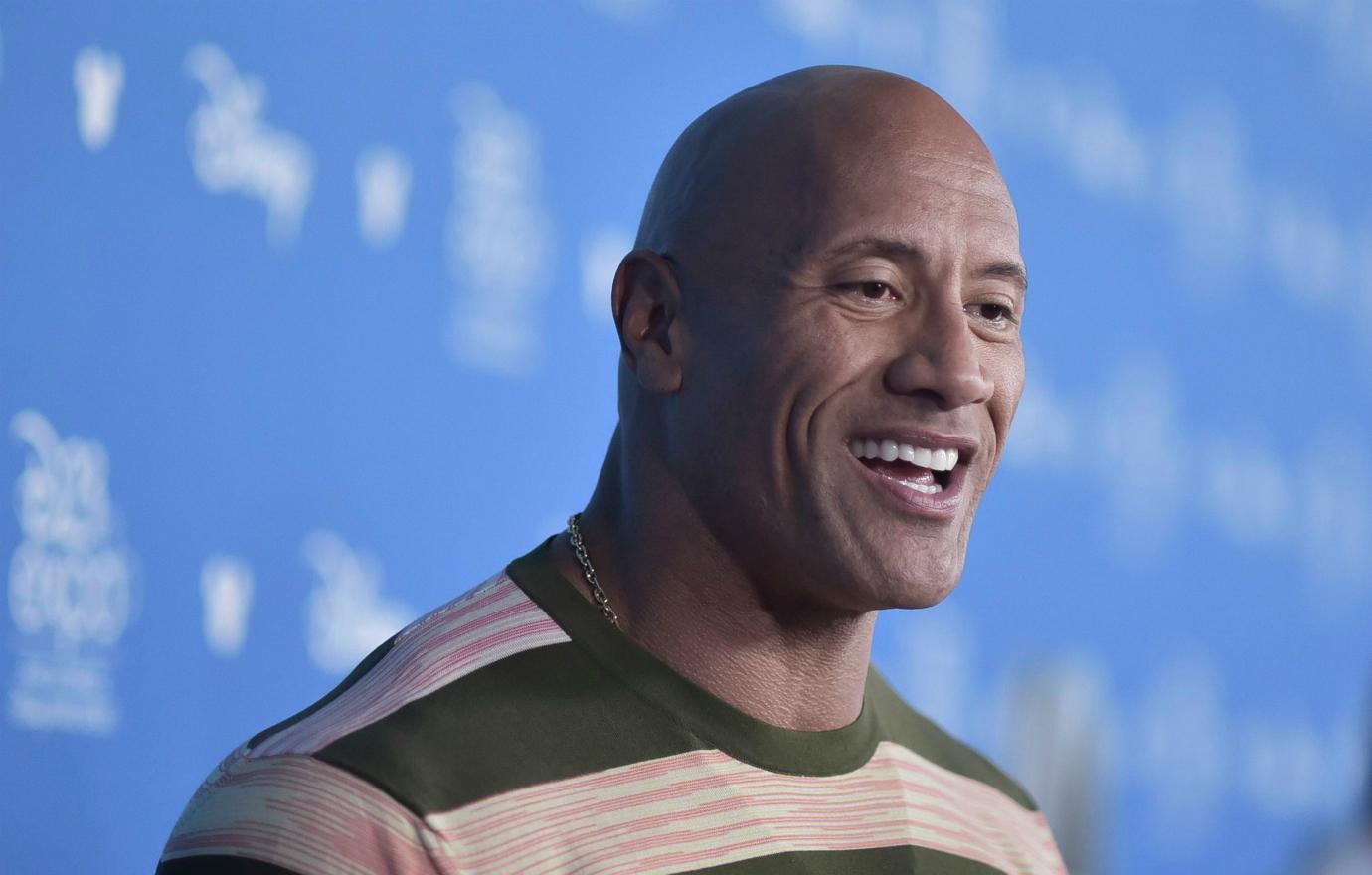 The Rock stands on the red carpet in a striped top.