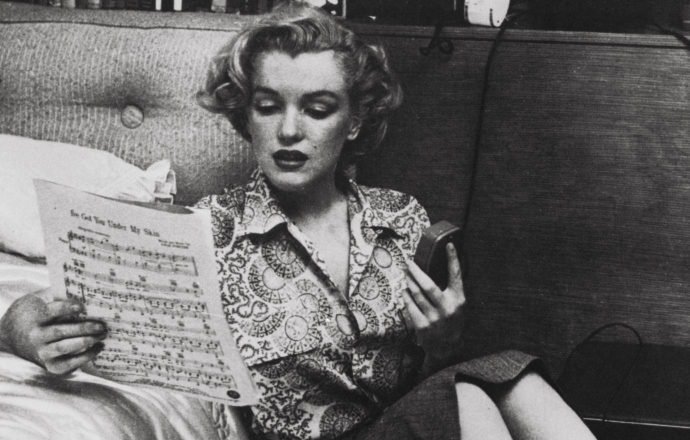 Marilyn Monroe looked over a piece of music in a black and white photo that found the icon in a knee-length skirt and a circular patterned blouse.