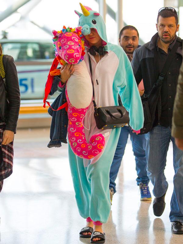 Miley Cyrus wears a unicorn onesie and holds a toy unicorn through Sydney Airport