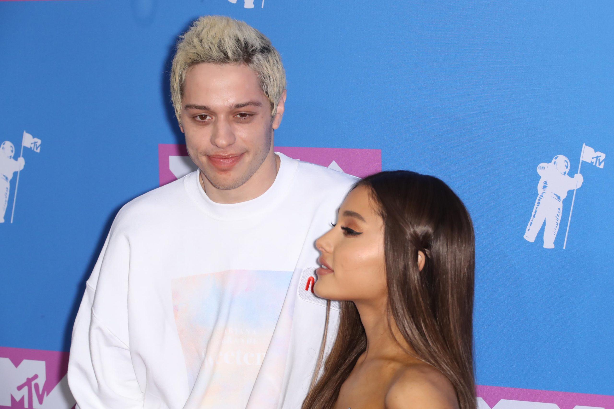 Pete Davidson in a white sweater and Ariana Grande