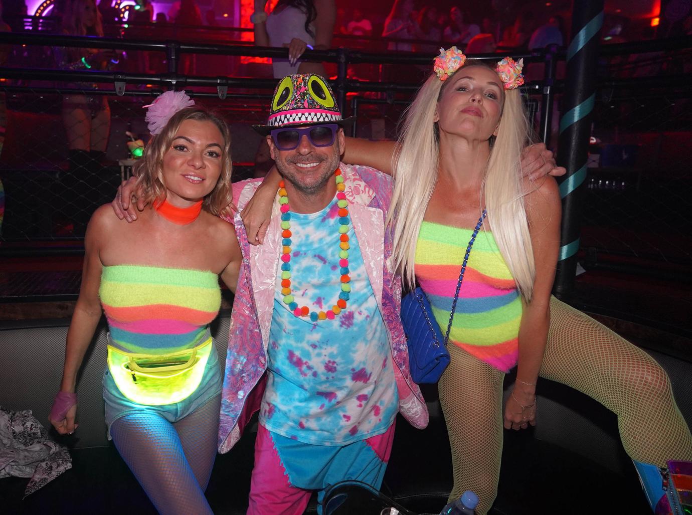 Guy Laliberté Wearng Colorful Neon Outfit Poses Smiling With Two Women In Neon Stripped Bodysuits and Fishnets