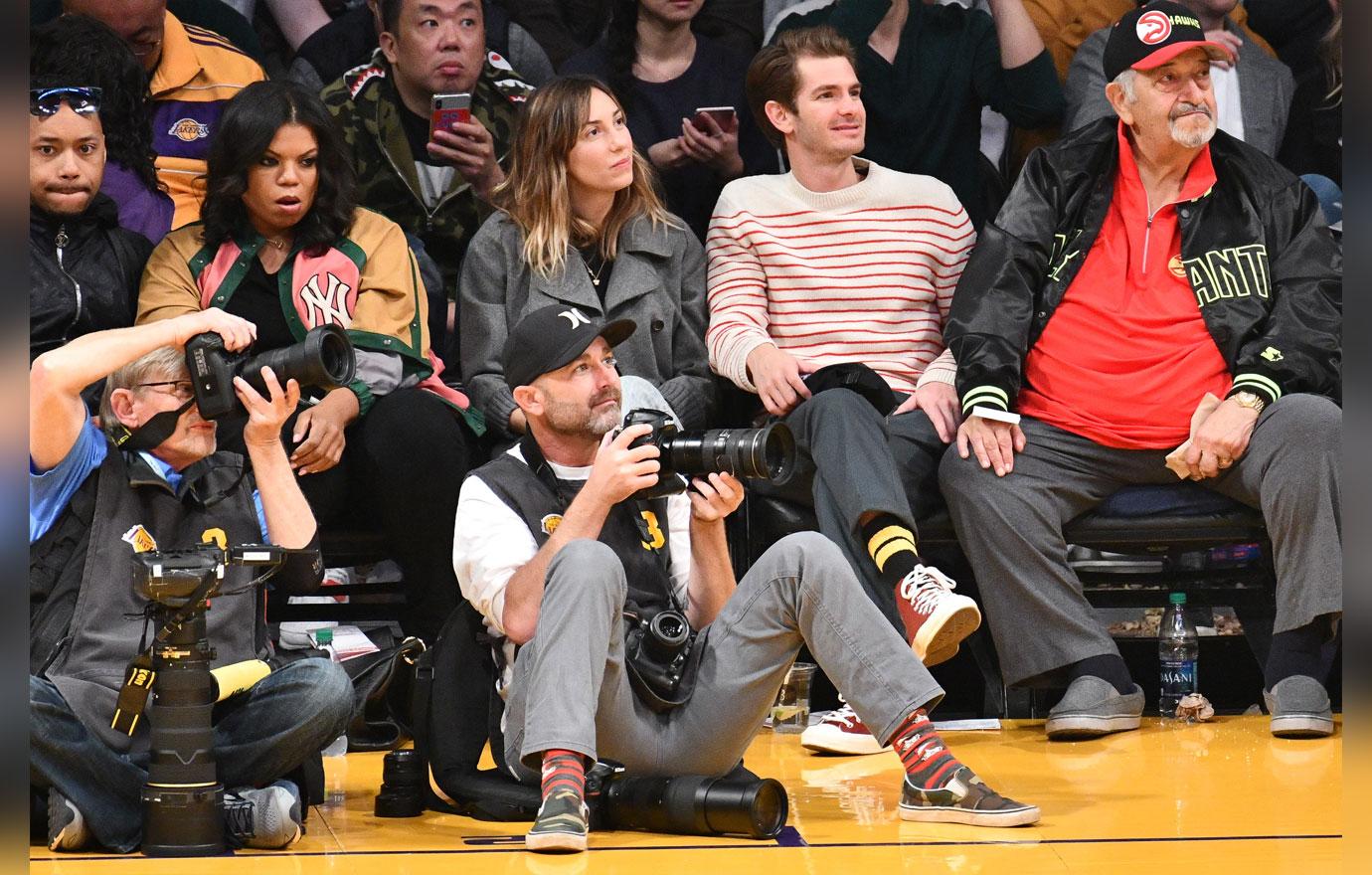 Andrew garfield in a striped sweater and a friend watching basketball.