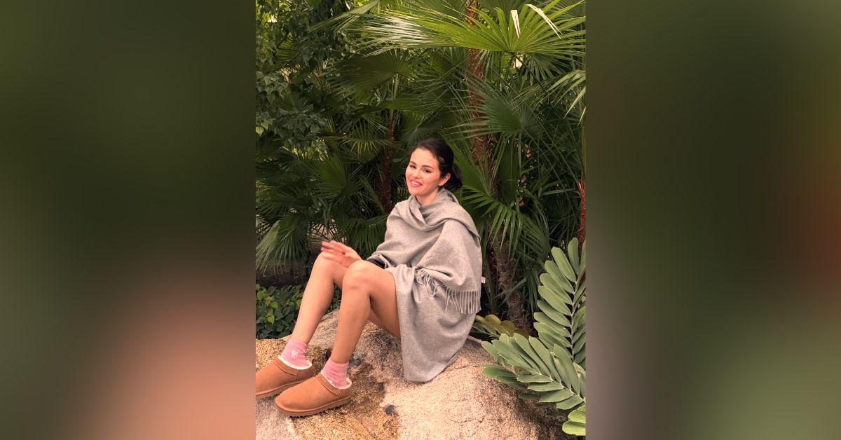 Image of Selena Gomez cozied up in a gray shall in the trees.