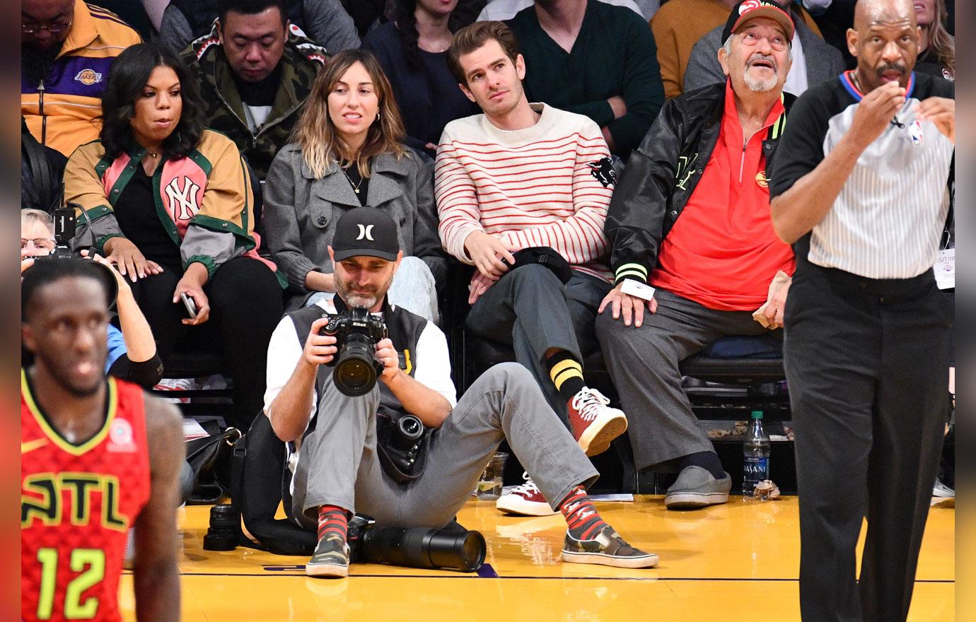 Andrew Garfield and his friend are smiling as they watch the Lakers Hawks game.