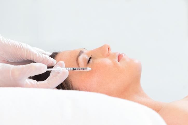 Young woman lying down receiving botox injection in her cheek