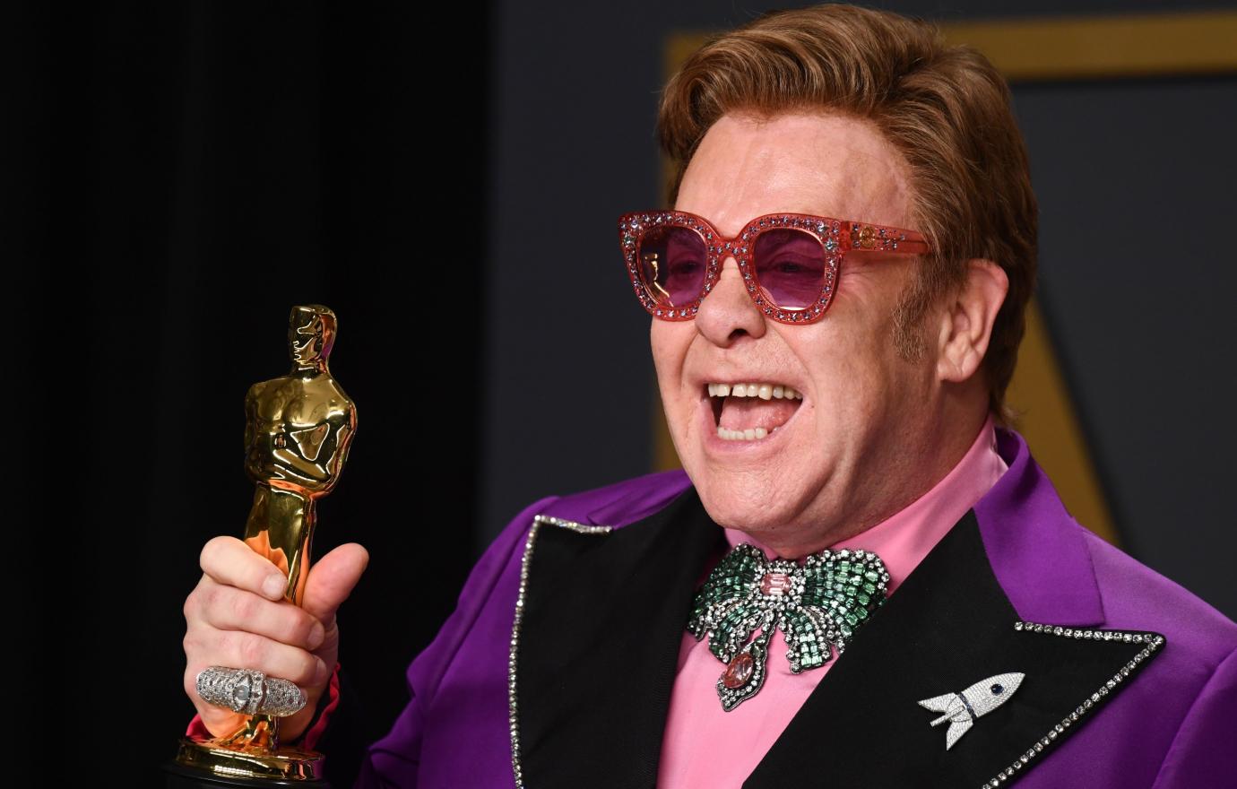 Elton John, as he showed off his Academy Award, wore a bejeweled purple tuxedo with a rocket lapel pin.