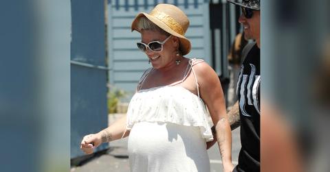 A very pregnant Pink walks down the street in a white dress and straw hat.