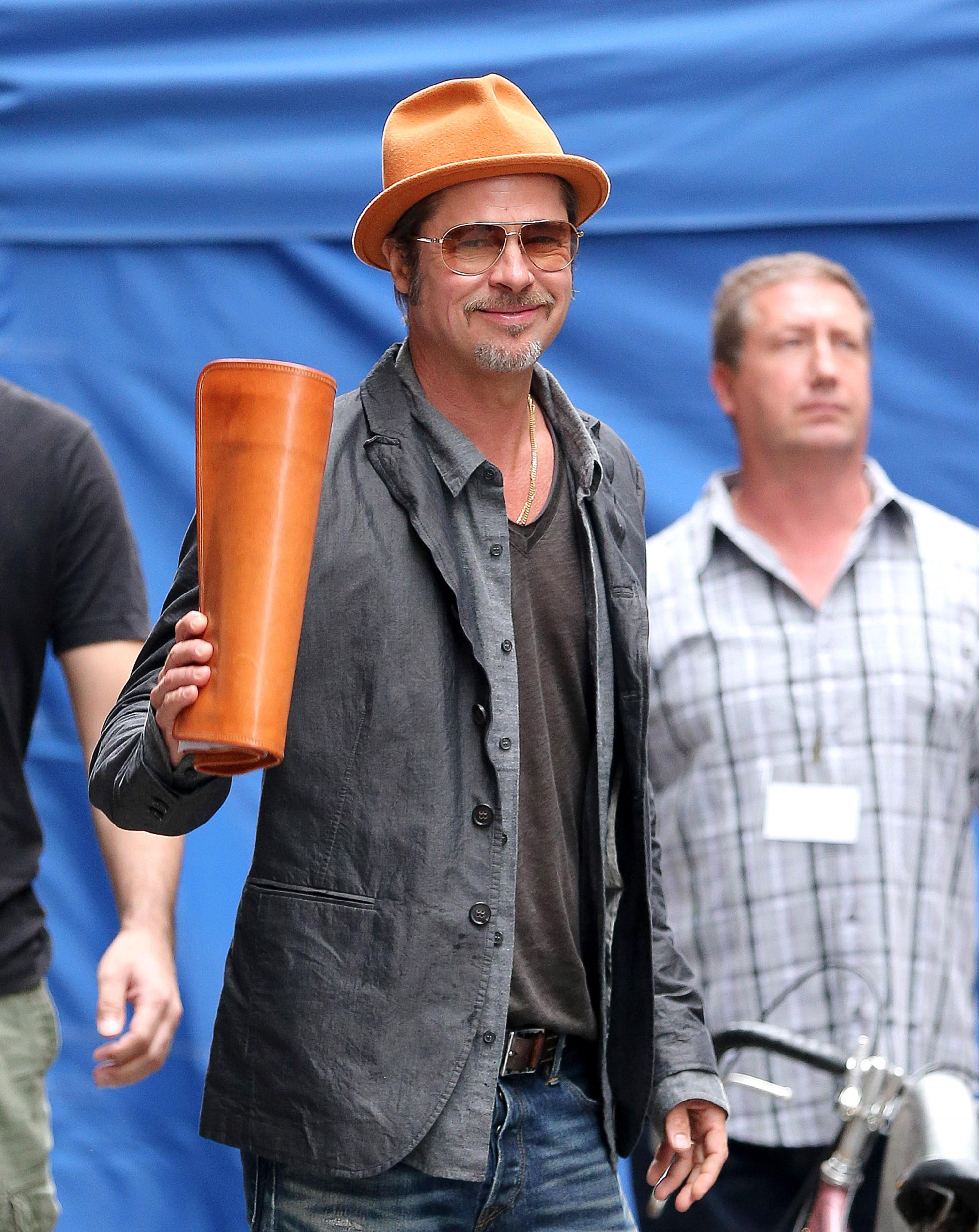 Brad Pitt flashes his big smile as he holds a orange leather folder matching with his fedora hat while arrives at the &#8221; RatPac &#8221; asian casino commercial in New York City