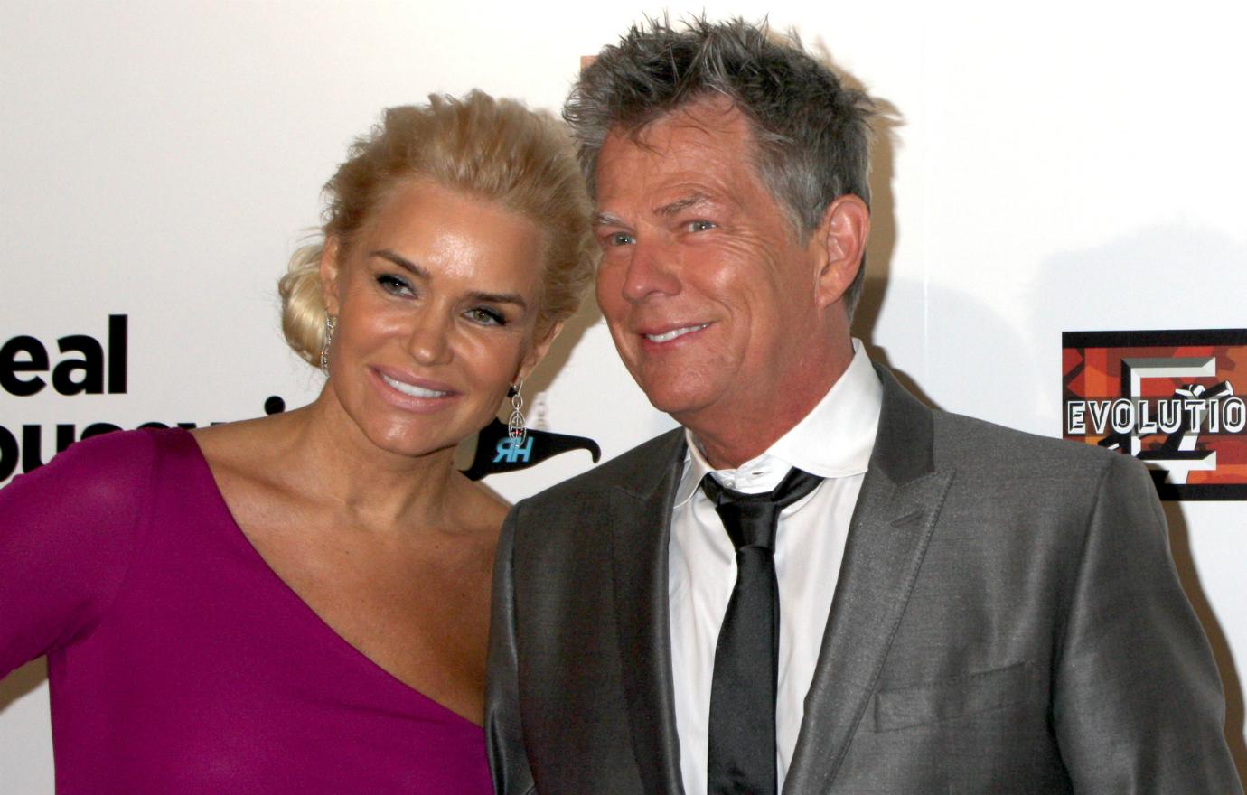 Yolanda Hadid wears a purple one shoulder dress with then-husband David Foster, wearing a gray suit, at the Real Housewives of Beverly Hills season three premiere event.