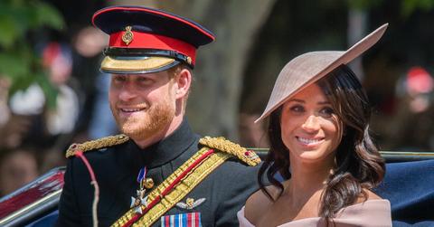Prince Harry, in royal garb and hat, sits in a carriage with Meghan Markle who wears a matching pink dress and hat.