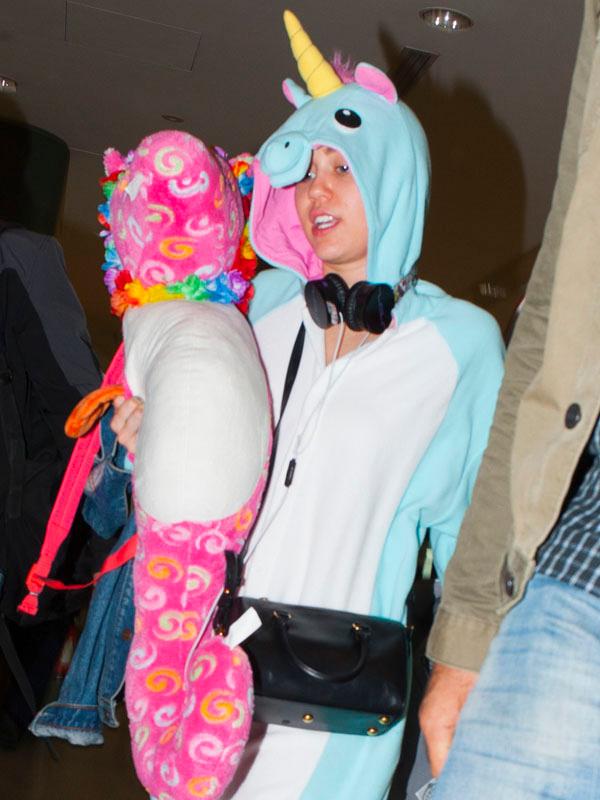 Miley Cyrus wears a onesie and carries a pink seahorse through Sydney Airport