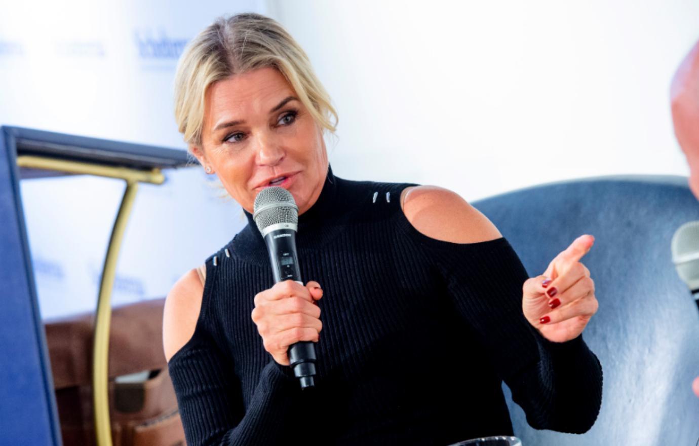 Yolanda wears a black shirt with shoulder cutouts, her hair pulled back, as she talks to the press about her book.