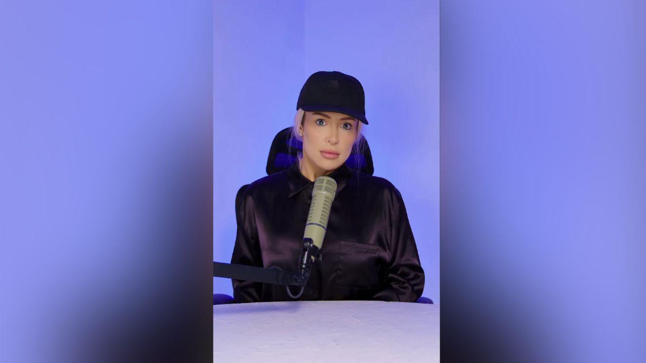 Image of The influencer wore a black baseball cap and dark blouse while sitting behind a podcast microphone.