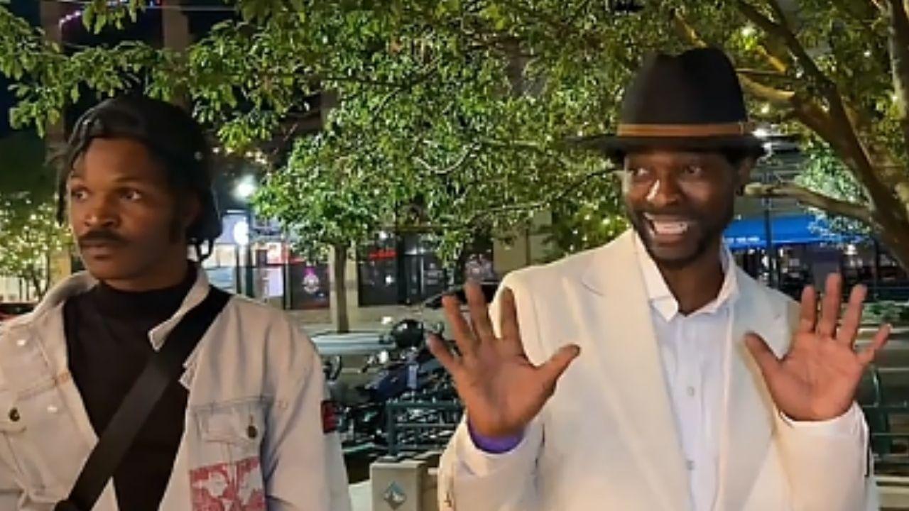 Image of On the sidewalk was a man in an all-white suit with a black hat, who approached the streamers, grinning widely.