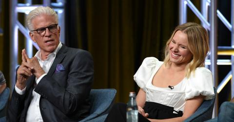 Kristin Bell sits on stage, laughing, as Ted Danson sits next to her watching.