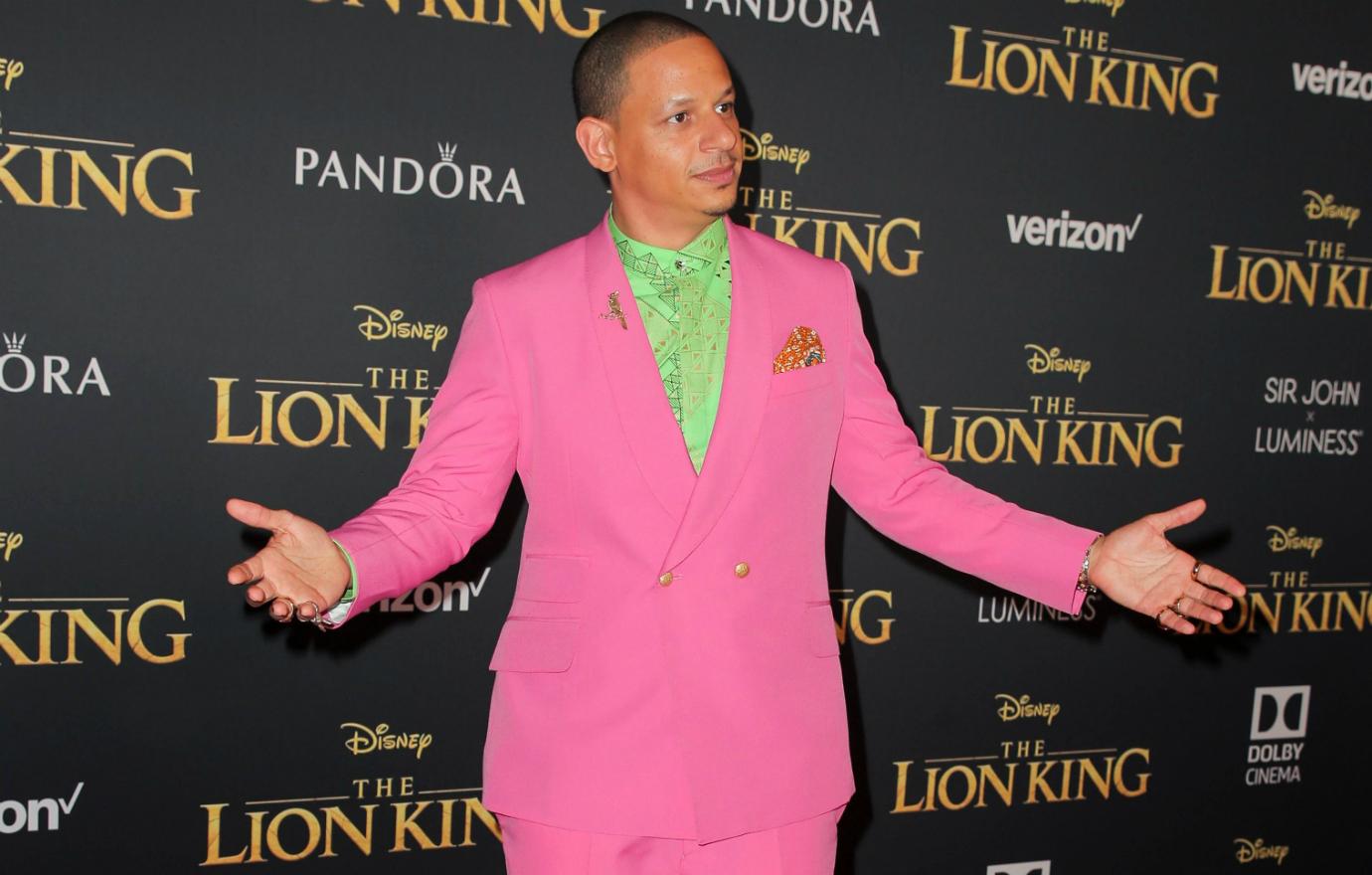 Eric Andre stands with hands outstretched in a bright pink suit and light green shirt.