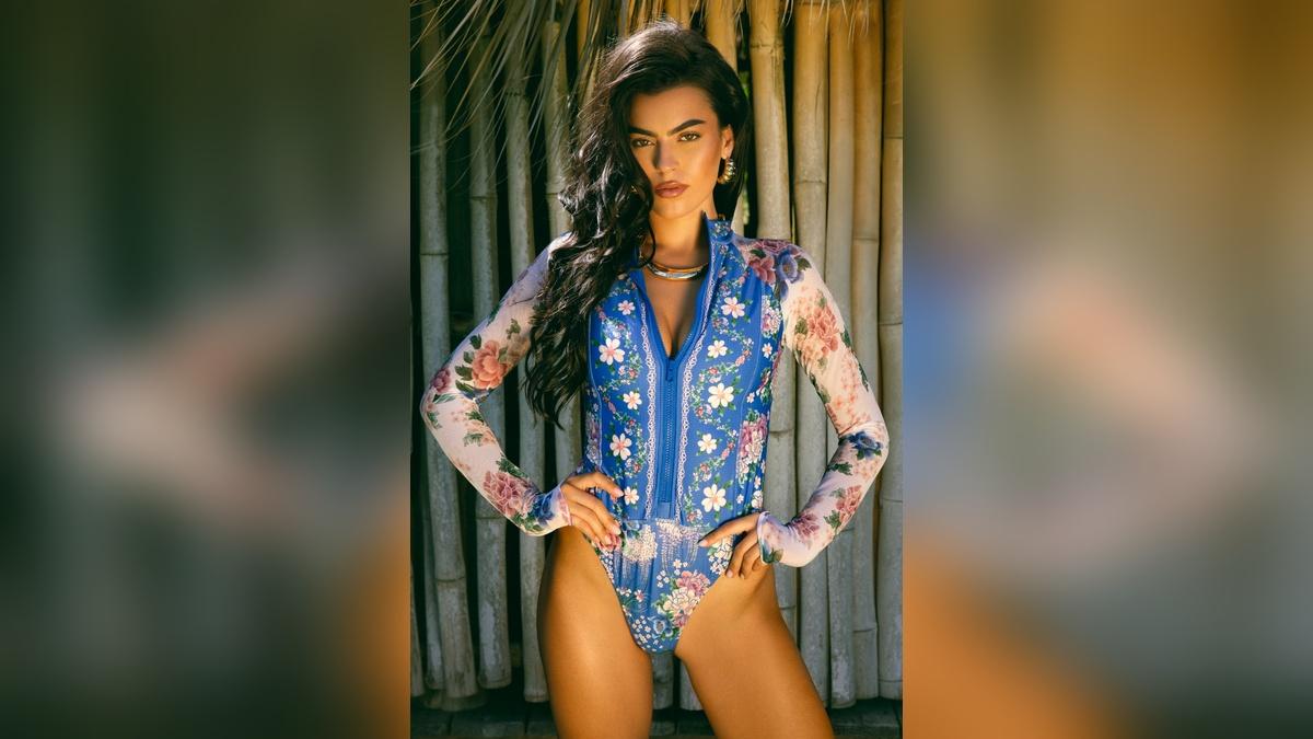 Image of Sarah Jane Nader stunned in a high-cut, long-sleeve blue swimsuit.