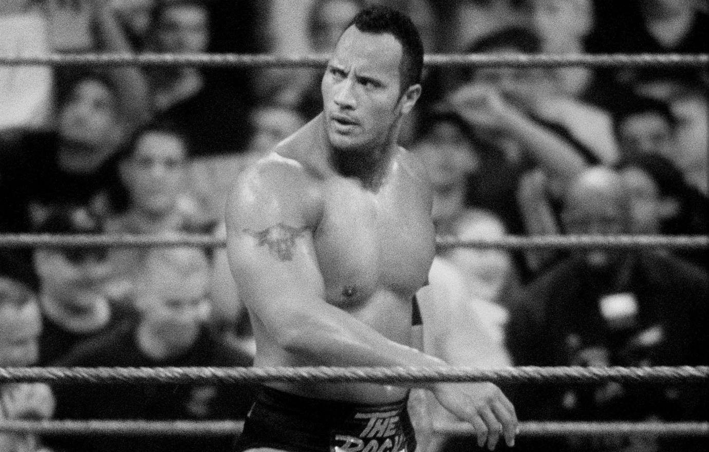 The Rock walks barechested around a wrestling ring.