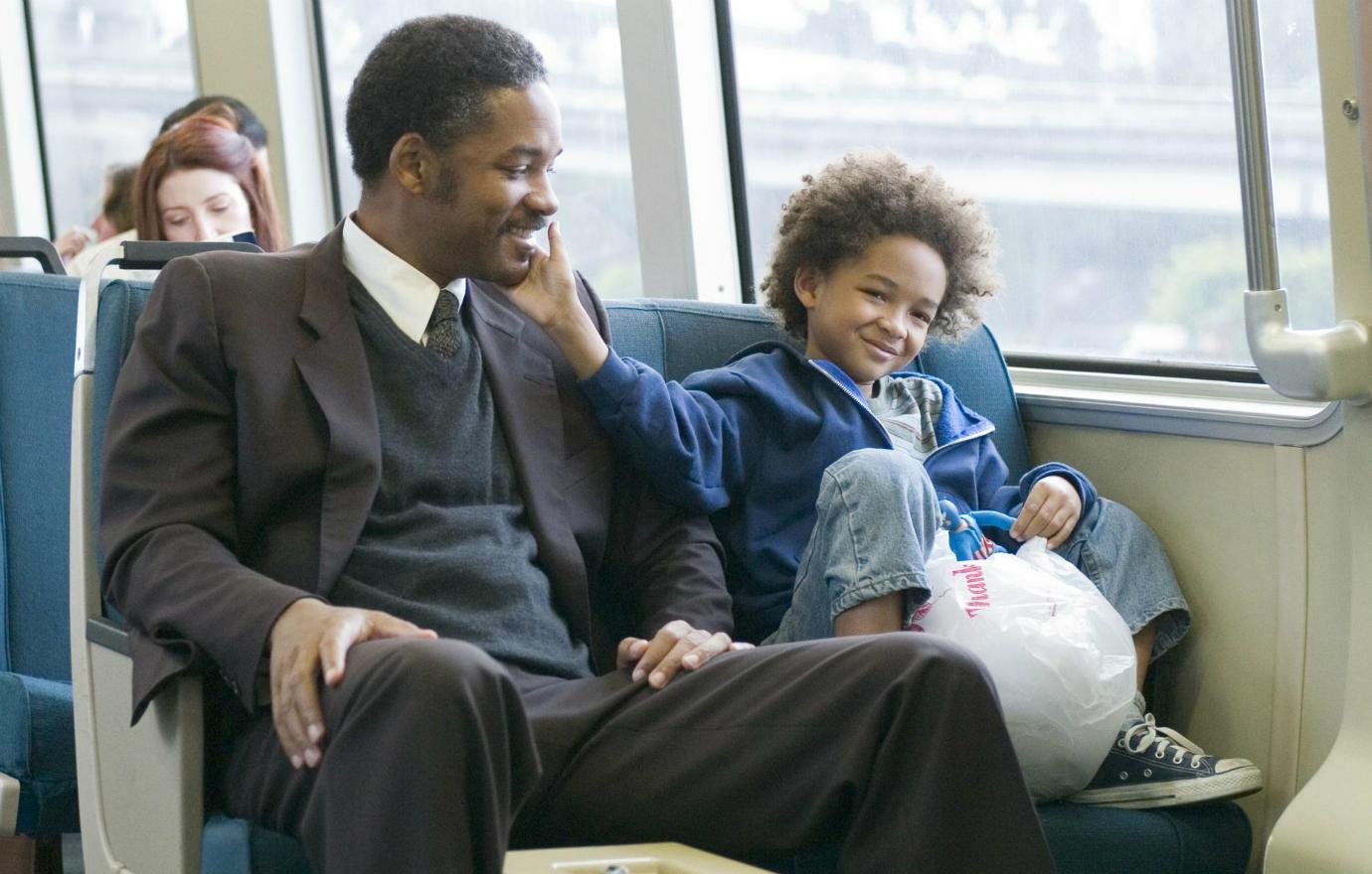 Will Smith, in a dark suit with a sweater vest, rode the subway with his son, Jaden Smith, who wore jeans and a blue jacket.