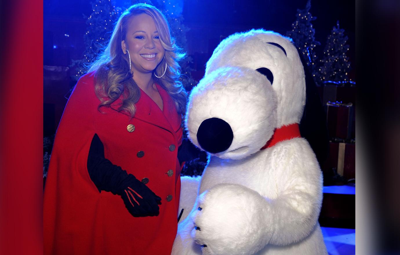 A pregnant Mariah Carey wears a red dress and black gloves and poses alongside a life-size Snoopy.