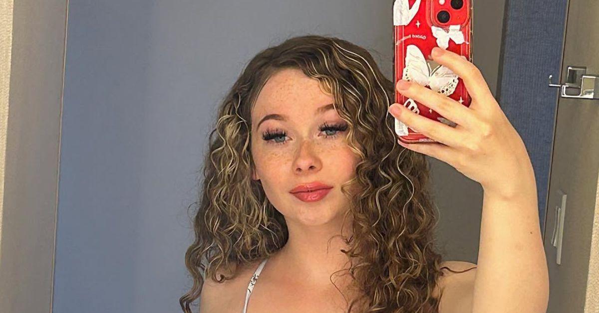 Vanessa Stevens snaps a mirror selfie in a bathroom, holding a red phone with a butterfly case.