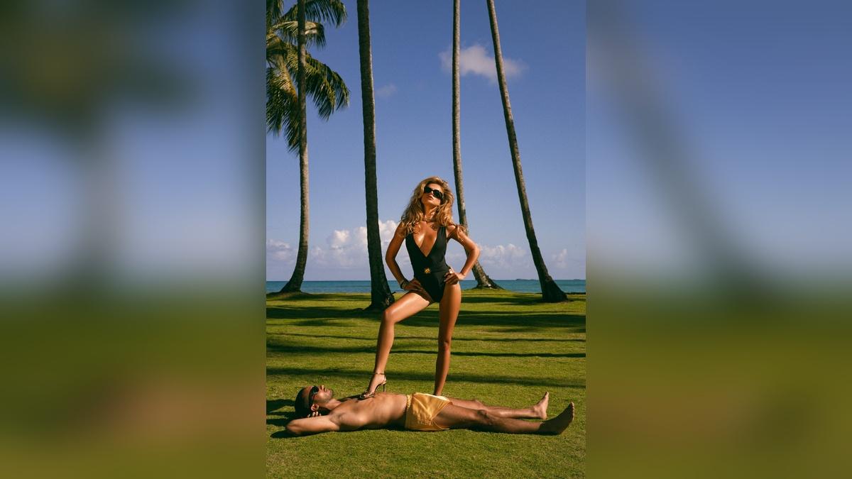 Image of Brooks stepped on a man’s chest in a plunging black one-piece, radiating boss energy.