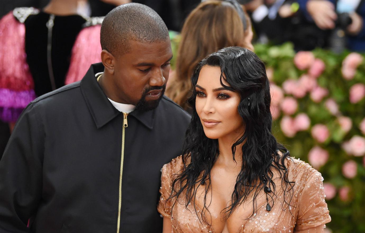 Kanye, in black, looks at Kim who wears a peach colored dress.