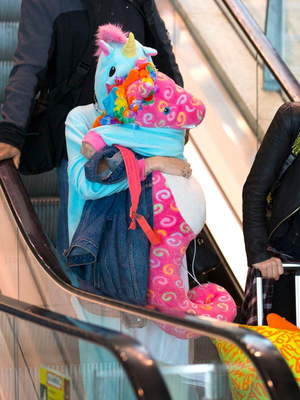 Miley Cyrus wears a onesie and carries a pink seahorse through Sydney Airport