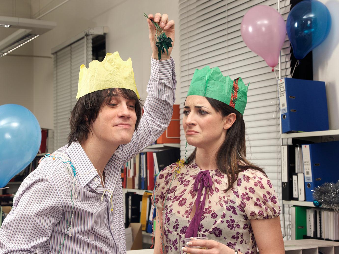 Male office worker holding mistletoe above female colleague