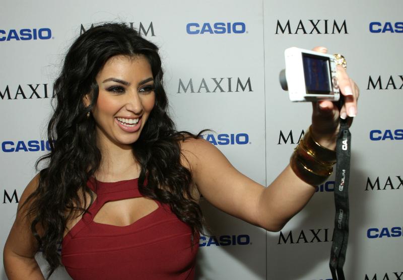 Kim Kardashian wears a red bandage dress and wavy long hair while taking a selfie at this 2007 Maxim Style Awards event.