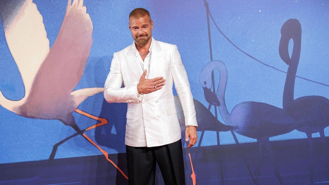Image of Ricky Martin wore a white double-breasted jacket over wide-leg black slacks, topping off his look with a signature silver chain around his neck and a pair of purple-tinted shades.