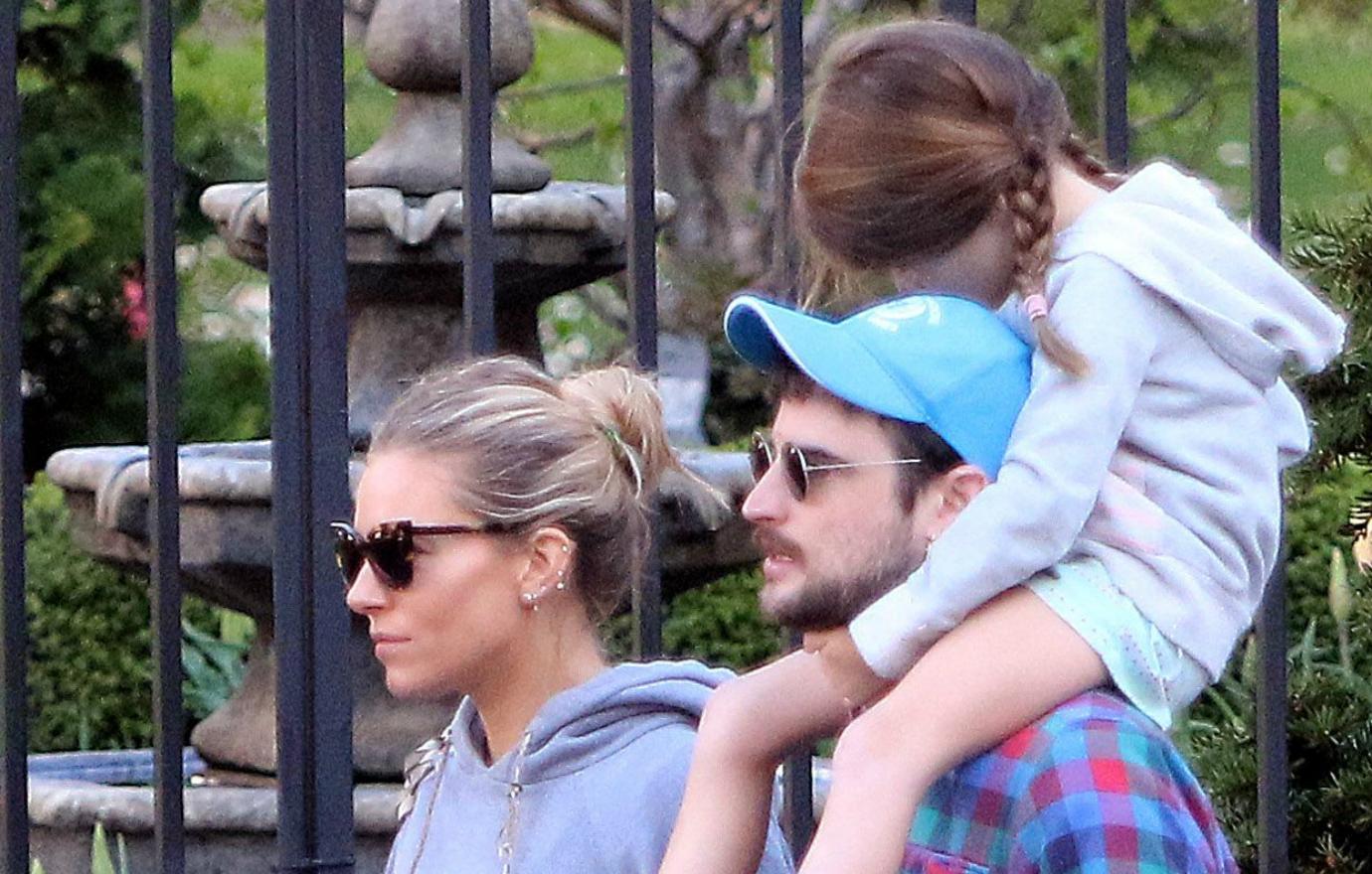 Sienna and Tom walk together with their kid on Tom's shoulders.