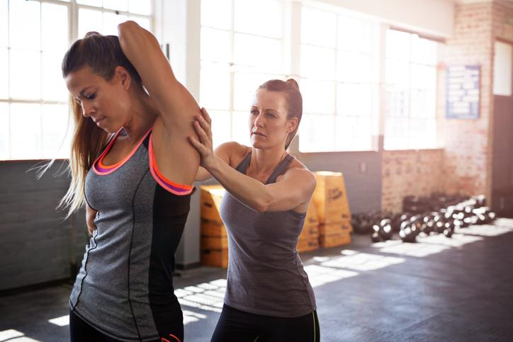 Woman assisting friend with stretch after training session at gym gym