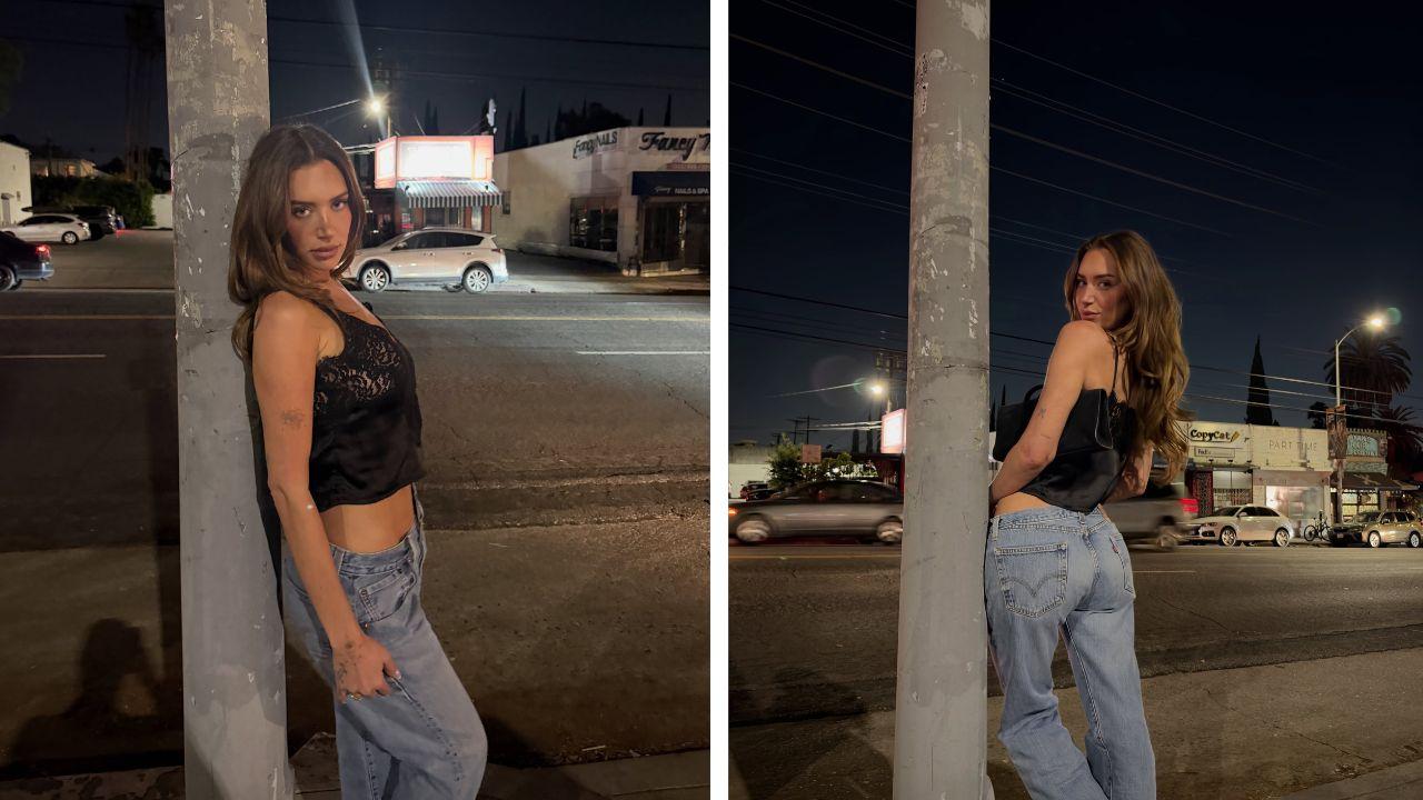 Image of The influencer posed in a black lace camisole and baggy jeans while leaning against a pole during a night out.